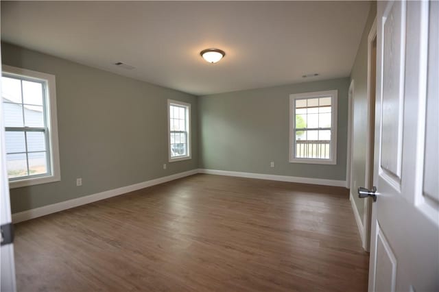 unfurnished room with visible vents, dark wood finished floors, and baseboards