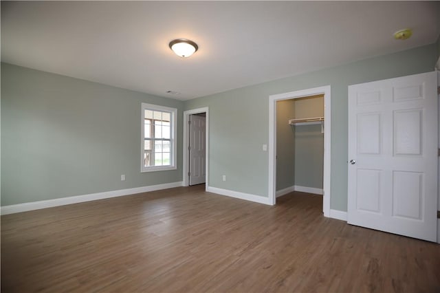 unfurnished bedroom with a closet, a spacious closet, baseboards, and wood finished floors