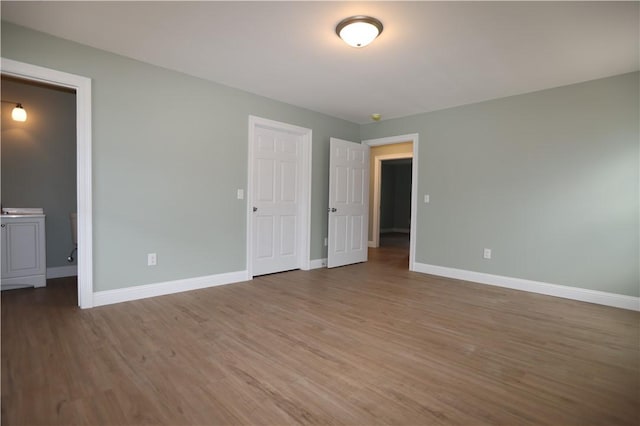 unfurnished bedroom featuring ensuite bath, wood finished floors, and baseboards