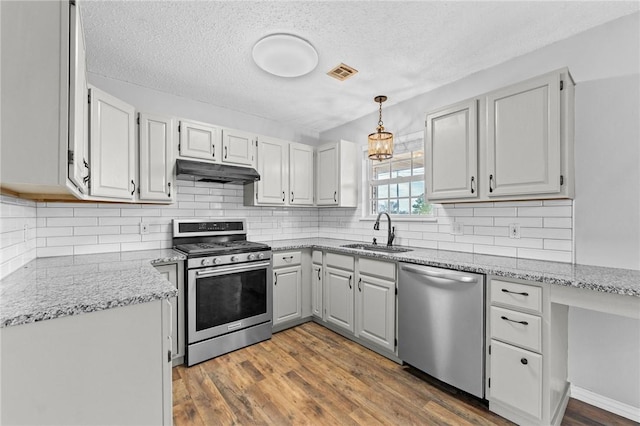 kitchen with under cabinet range hood, stainless steel appliances, a sink, visible vents, and dark wood-style floors