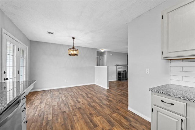 unfurnished dining area featuring a textured ceiling, a notable chandelier, visible vents, baseboards, and dark wood finished floors