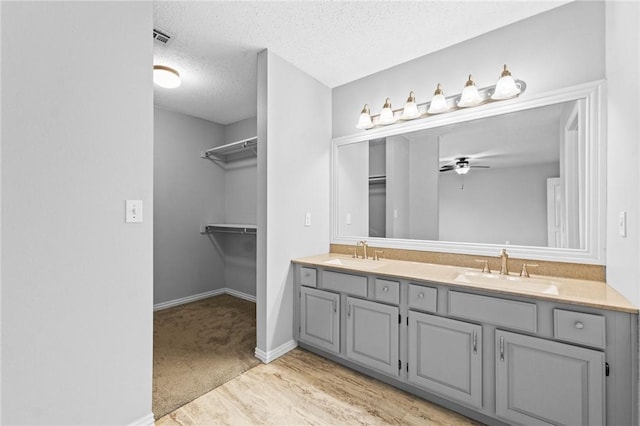 bathroom featuring a textured ceiling, double vanity, a sink, and a walk in closet