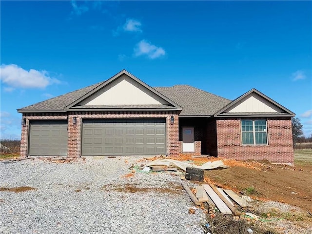 ranch-style house with a shingled roof, gravel driveway, brick siding, and an attached garage