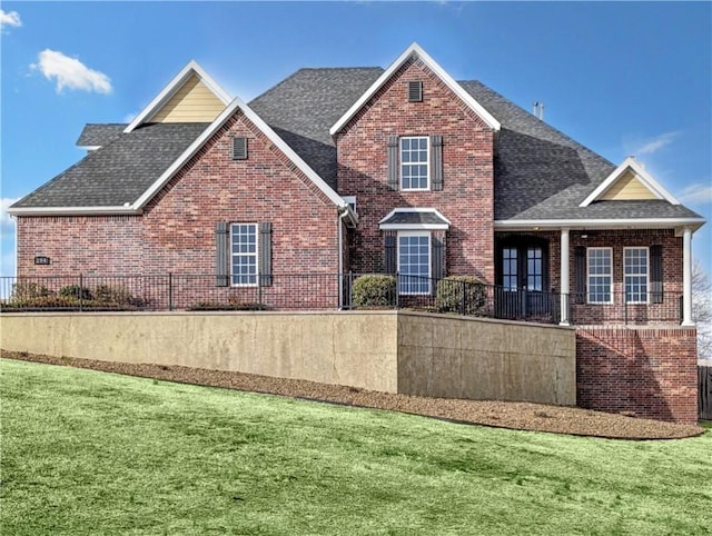 view of front of home featuring a shingled roof, brick siding, and a front lawn