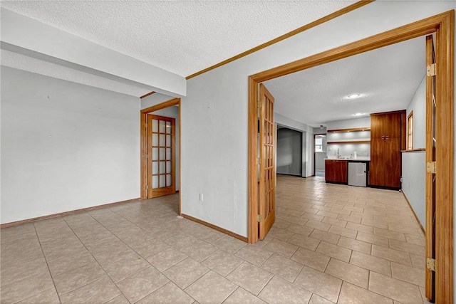 empty room featuring a textured ceiling, light tile patterned flooring, a sink, and baseboards