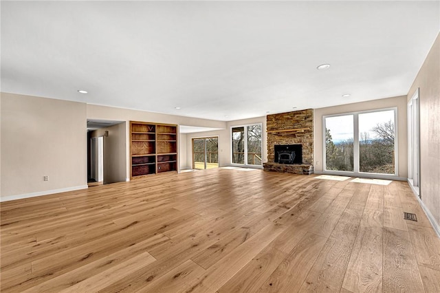 unfurnished living room featuring visible vents, baseboards, built in shelves, light wood-style floors, and a fireplace