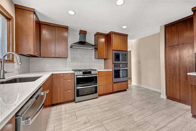 kitchen featuring tasteful backsplash, wall chimney exhaust hood, appliances with stainless steel finishes, light stone countertops, and a sink