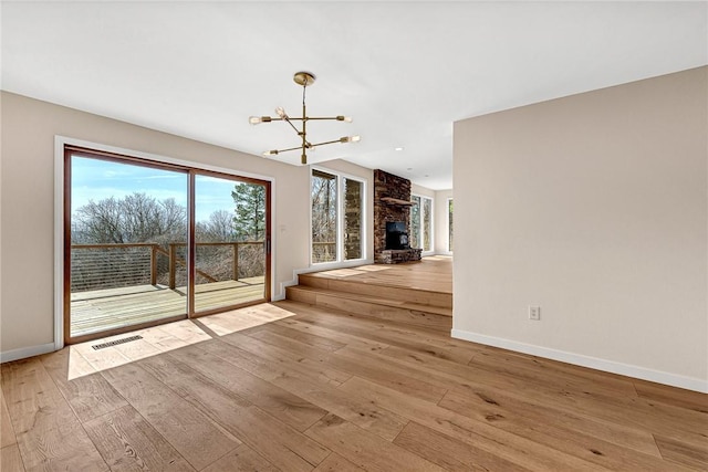 spare room featuring a chandelier, a large fireplace, visible vents, and hardwood / wood-style flooring