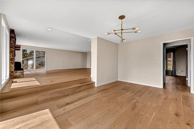 unfurnished living room featuring baseboards, light wood-style flooring, and a notable chandelier