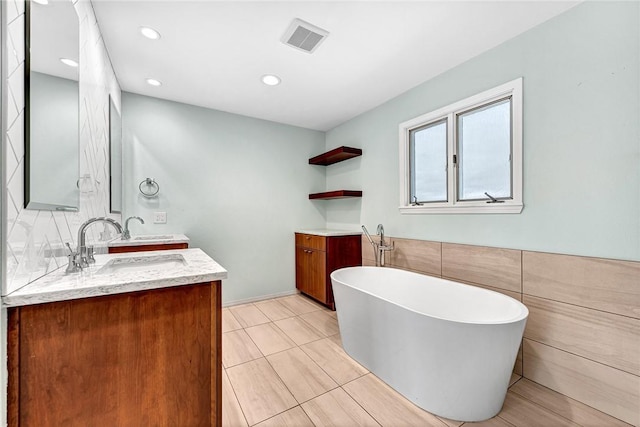 bathroom featuring double vanity, visible vents, a freestanding tub, a sink, and recessed lighting