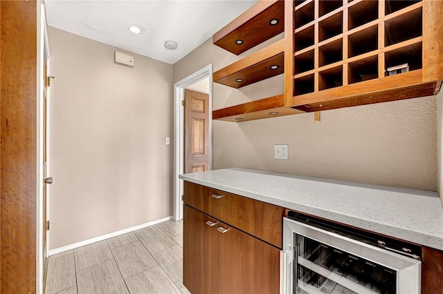 kitchen featuring wine cooler, light stone counters, baseboards, open shelves, and brown cabinetry