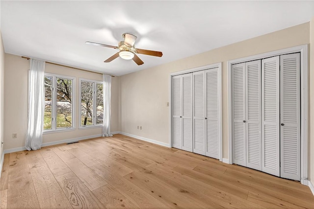 unfurnished bedroom featuring light wood finished floors, two closets, visible vents, and baseboards