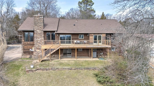 rear view of house with a shingled roof, a lawn, a chimney, stairs, and a deck