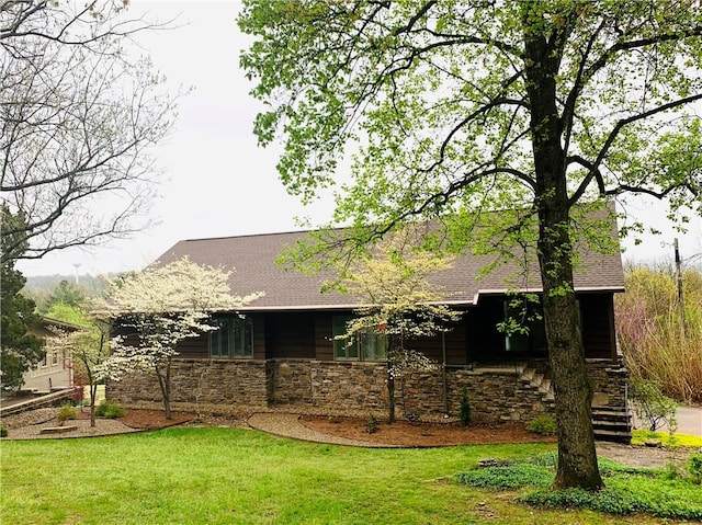 view of front of house with stairs, stone siding, roof with shingles, and a front yard