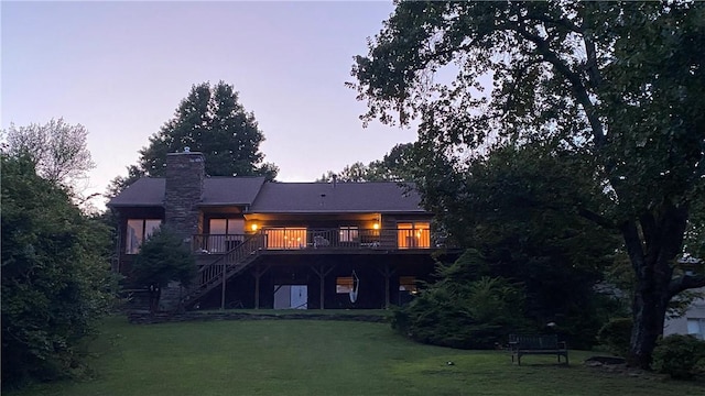 back of house at dusk with stairs, a yard, a chimney, and a wooden deck