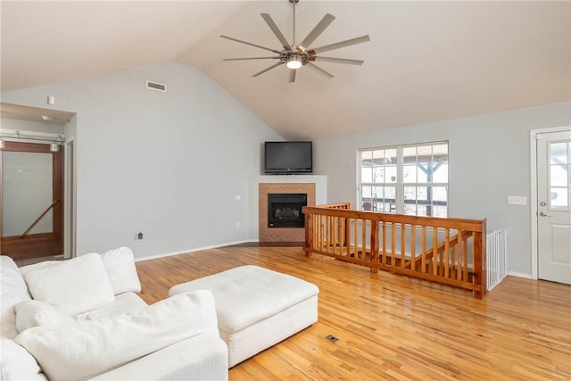 living room featuring light wood-style floors, lofted ceiling, visible vents, and a tiled fireplace