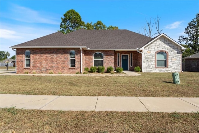 single story home featuring stone siding, roof with shingles, brick siding, and a front yard