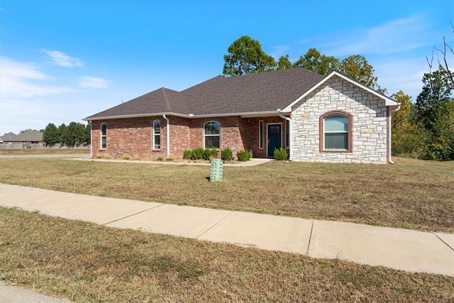 ranch-style house featuring brick siding, a shingled roof, stone siding, and a front yard