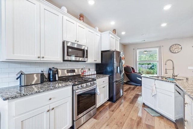 kitchen featuring stainless steel appliances, light wood-style flooring, decorative backsplash, white cabinets, and a sink