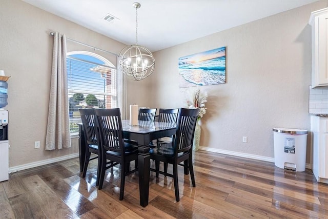 dining space with baseboards, wood finished floors, visible vents, and a notable chandelier