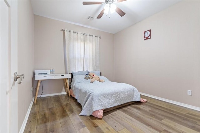 bedroom with a ceiling fan, wood finished floors, visible vents, and baseboards