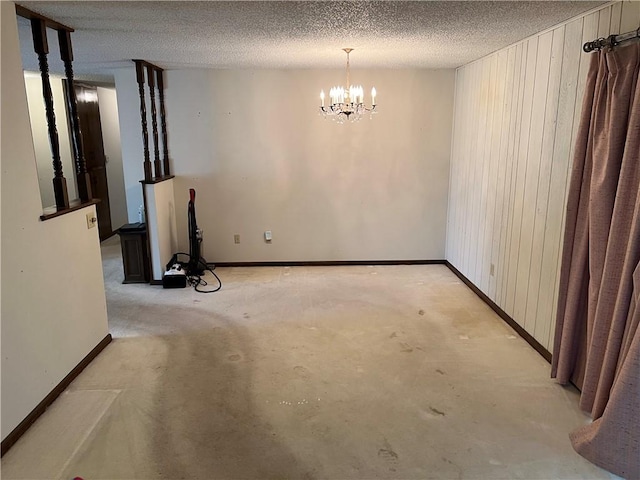 empty room with wood walls, baseboards, a chandelier, and a textured ceiling