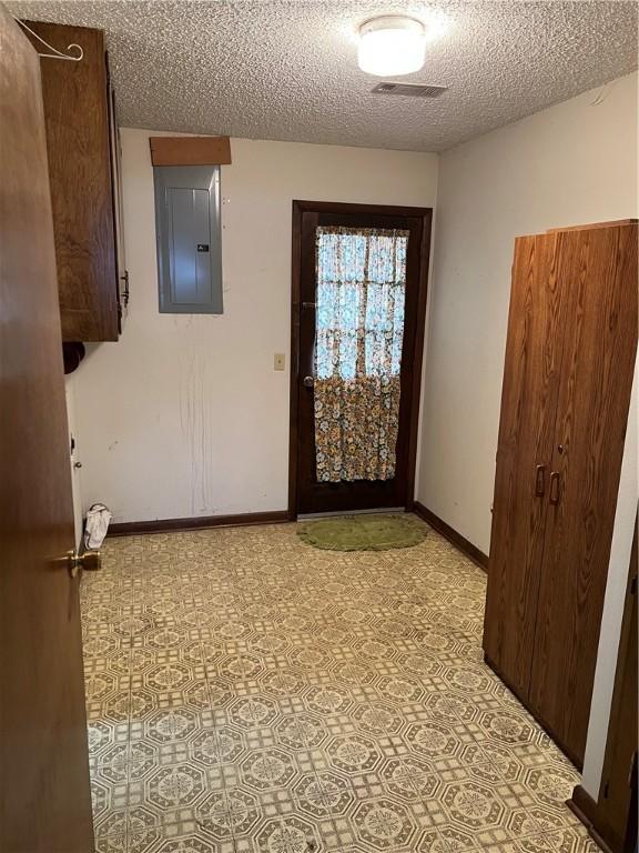 interior space with a textured ceiling, visible vents, electric panel, and baseboards