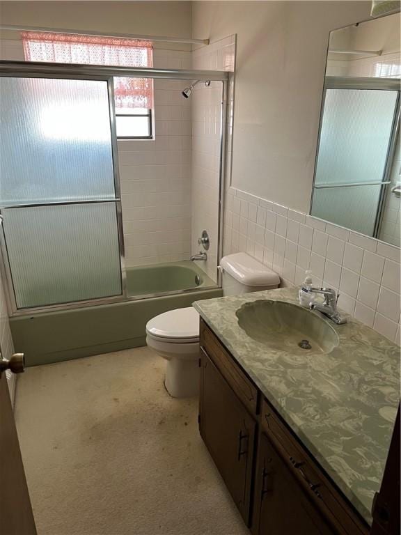 bathroom featuring bath / shower combo with glass door, wainscoting, toilet, vanity, and tile walls