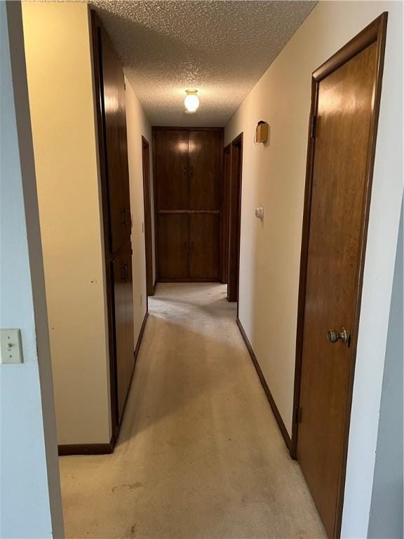 hall with light carpet, baseboards, and a textured ceiling