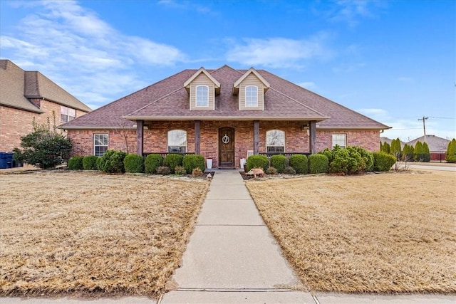 view of front of home featuring brick siding, a front lawn, a porch, and a shingled roof