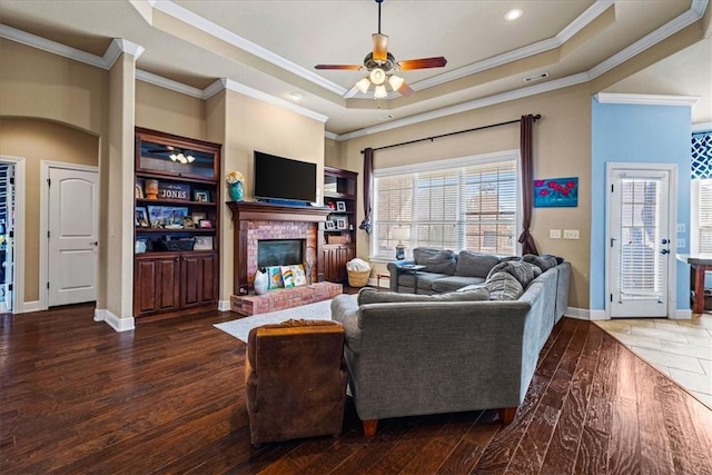 living room featuring arched walkways, a fireplace, wood finished floors, baseboards, and a raised ceiling