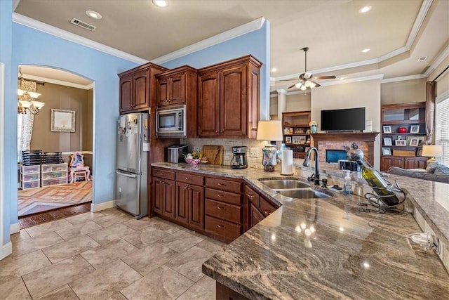 kitchen with stainless steel appliances, a sink, open floor plan, tasteful backsplash, and dark stone countertops