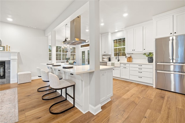 kitchen featuring a fireplace, light wood-style floors, white cabinets, freestanding refrigerator, and island exhaust hood