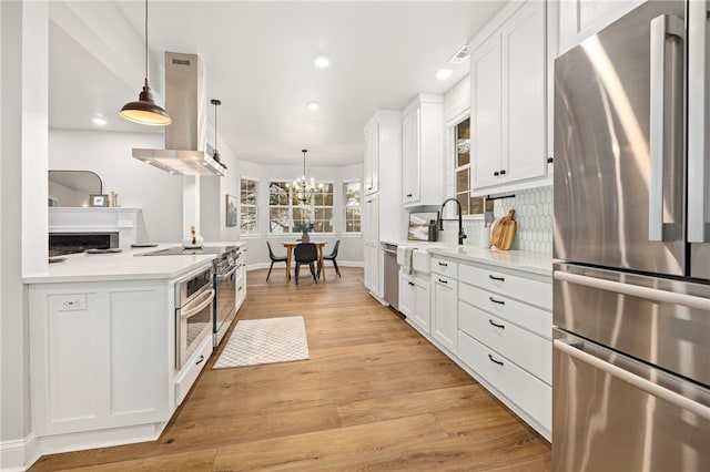 kitchen featuring stainless steel appliances, a sink, white cabinetry, light countertops, and island exhaust hood