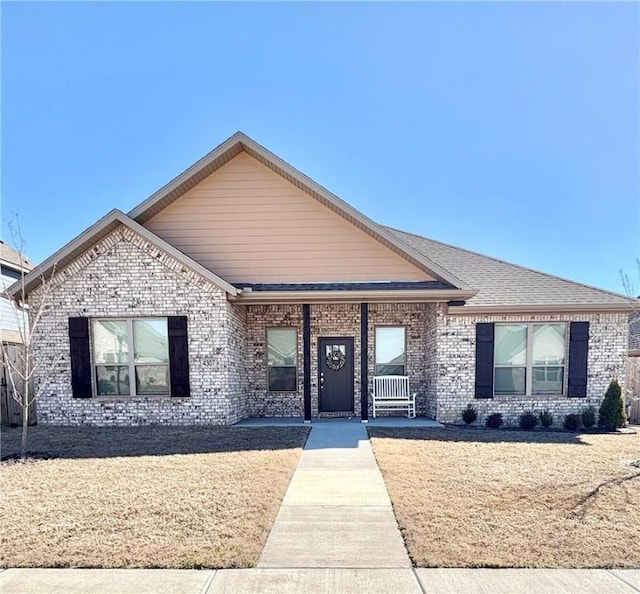 ranch-style house with roof with shingles, a front yard, and brick siding