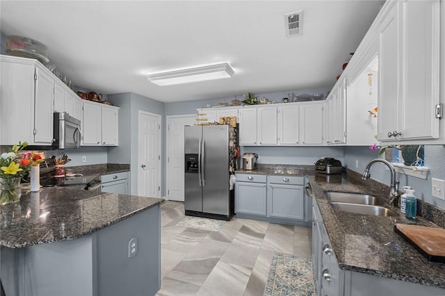 kitchen with dark stone countertops, stainless steel appliances, a peninsula, and a sink