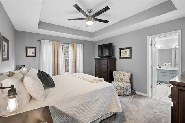 bedroom with a tray ceiling, visible vents, light carpet, ensuite bath, and baseboards