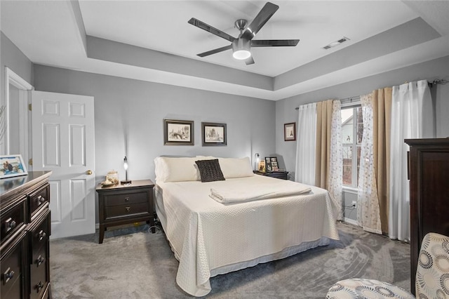 carpeted bedroom with a tray ceiling, visible vents, and a ceiling fan