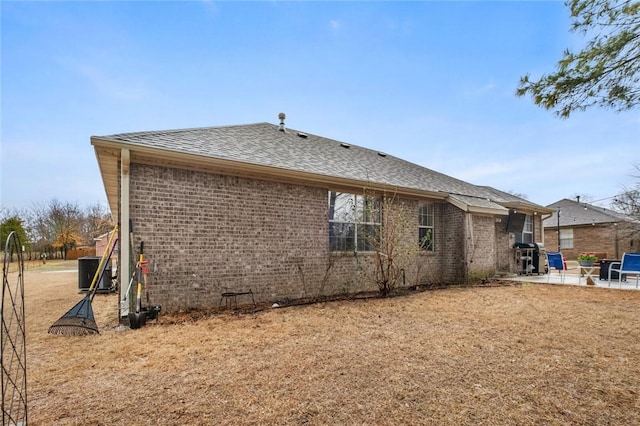 rear view of property with brick siding, a patio, central AC, and roof with shingles