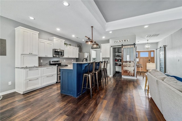 kitchen with a barn door, a kitchen bar, appliances with stainless steel finishes, and white cabinets