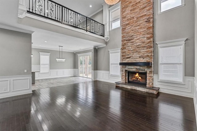 unfurnished living room with wainscoting, ornamental molding, wood-type flooring, and a fireplace