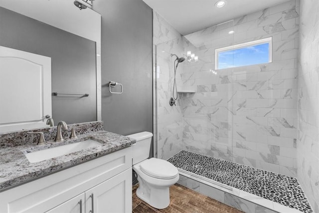 bathroom with vanity, wood finished floors, a tile shower, and toilet