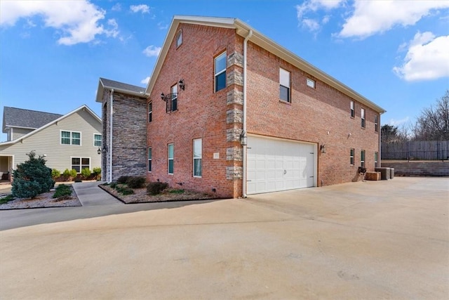 view of side of home featuring driveway, a garage, cooling unit, and brick siding