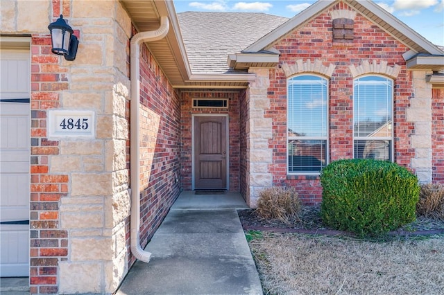 property entrance with a garage, brick siding, and a shingled roof