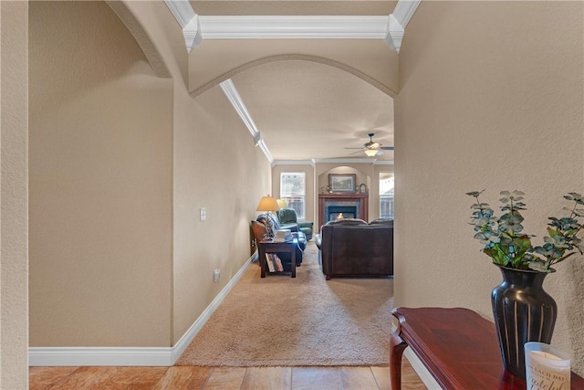 hallway featuring arched walkways, a textured wall, ornamental molding, and baseboards