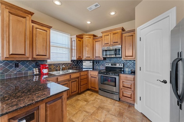 kitchen featuring visible vents, brown cabinetry, decorative backsplash, stainless steel appliances, and a sink