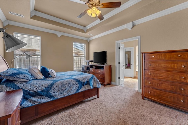 bedroom with a tray ceiling, light colored carpet, visible vents, ornamental molding, and ensuite bath