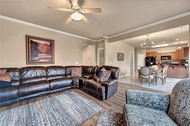 living room featuring baseboards, ornamental molding, ceiling fan with notable chandelier, and light wood-style floors