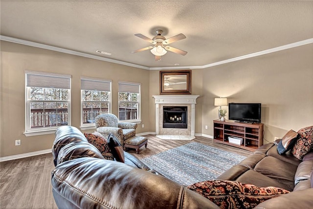 living area featuring a tiled fireplace, a ceiling fan, baseboards, wood finished floors, and visible vents