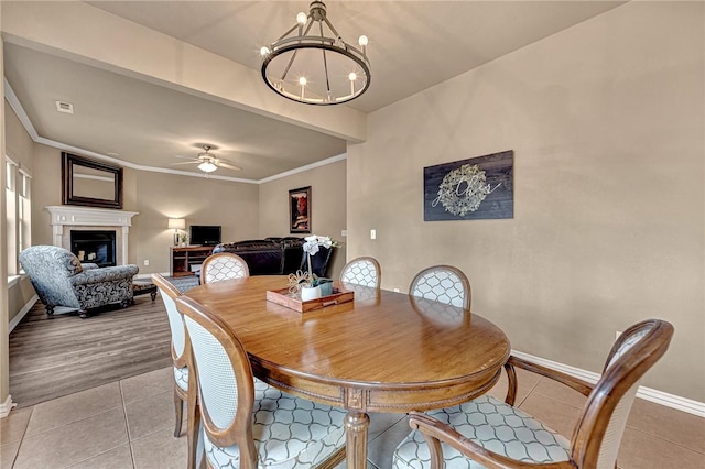 dining space featuring baseboards, a fireplace, ceiling fan with notable chandelier, and light tile patterned flooring